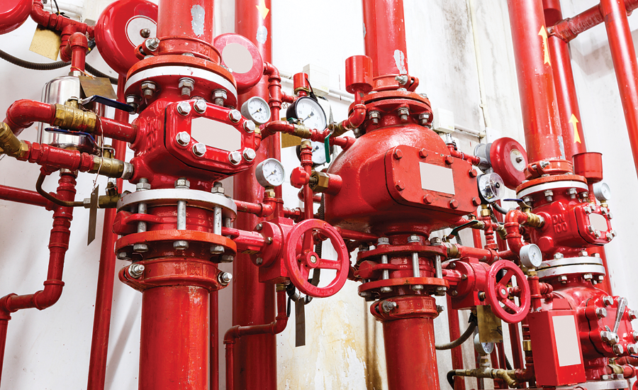 A complex arrangement of red industrial pipes, valves, and gauges mounted on a wall inside a building. The pipes are interconnected, and several pressure meters and control wheels are visible. The overall setup appears to be part of a fire suppression or hydrant system.